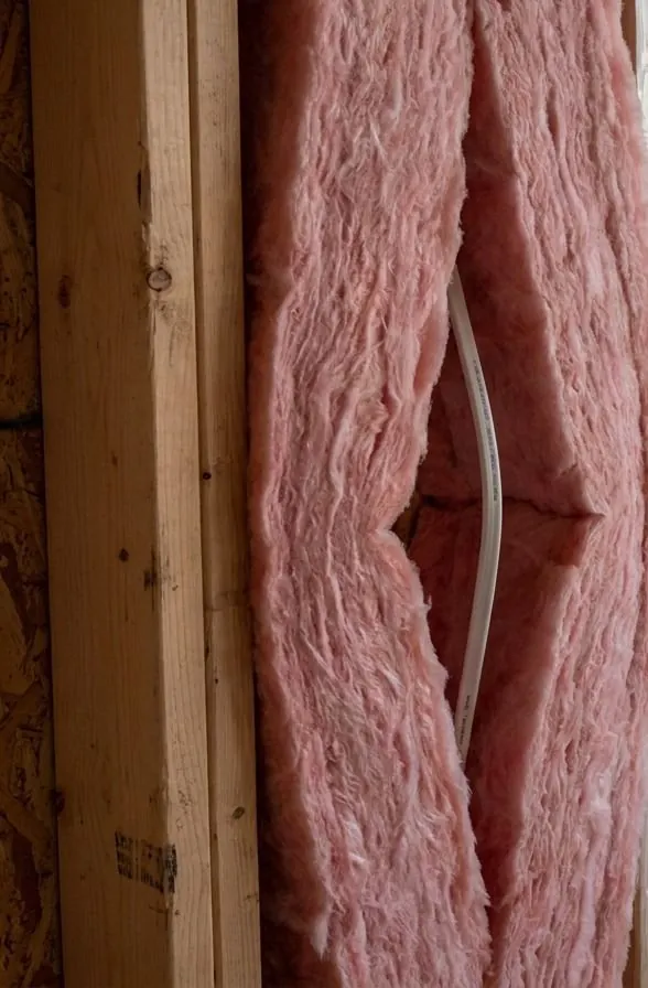 A pink fiberglass batt peeled open through its thickness, with a white electrical cable running inside the split instead of compressing the batt.