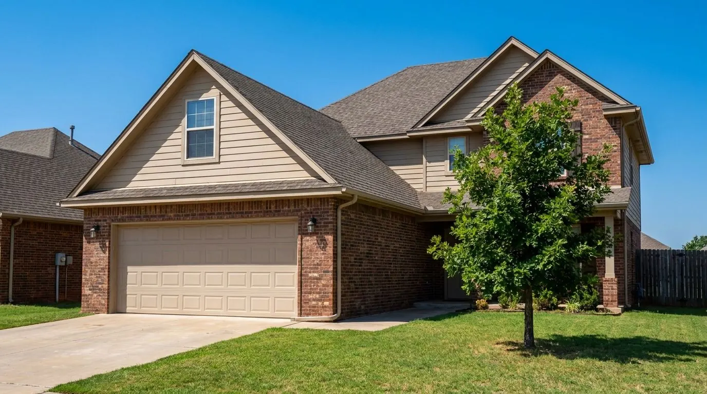A two-story suburban house with brick on the lower floor and siding above, and a bonus room built over the attached two-car garage, under a clear summer sky.